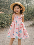 Smiling girl in a butterfly-patterned dress and straw hat, standing outdoors on a sunny day.