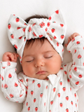 Baby girl sleeping peacefully in a strawberry-patterned outfit and large matching headband.