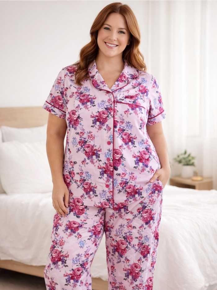 Woman smiling in floral pink pajamas, posing in a bright bedroom with soft, cozy bedding.