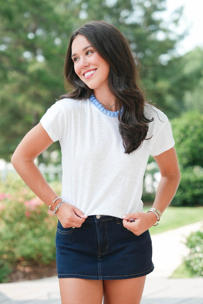 Woman wearing a white top and dark blue skirt outdoors with greenery in the background